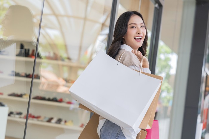 Happy smiling asian woman girls holding bunch of shopping bags,female returning home after shopping she bought many clothes at a reasonable price while discount  sales at store window display shop
