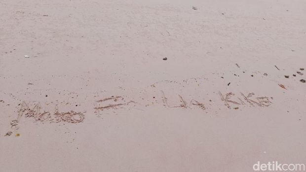 Keluarga menulis nama empat korban tenggelam Pinisi Putri Sakinah di pasir pink Pulau Padar, Taman Nasional Komodo, Kamis (1/1/2026).