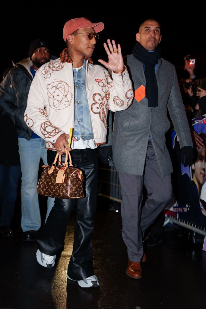 PARIS, FRANCE - JANUARY 24: Pharrell Williams wears a cap hat, a pale pastel pink jacket with floral print, a blue denim jacket , black flared leather pants , a brown Vuitton leather monogram print bag, outside the Kenzo Menswear Fall-Winter 2025/2026 show as part of Paris Fashion Week on January 24, 2025 in Paris, France. (Photo by Edward Berthelot/Getty Images)