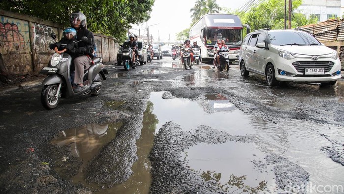 Kendaraan melintas di jalan berlubang yang tergenang air di Jalan Otista Raya, Ciputat, Minggu (4/1/2026).