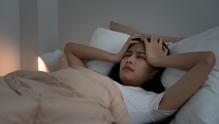 asian woman in bed late trying to sleep suffering insomnia, sleepless or scared in a nightmare, looking sad worried and stressed. Tired and headache or migraine waking up in the middle of the night.