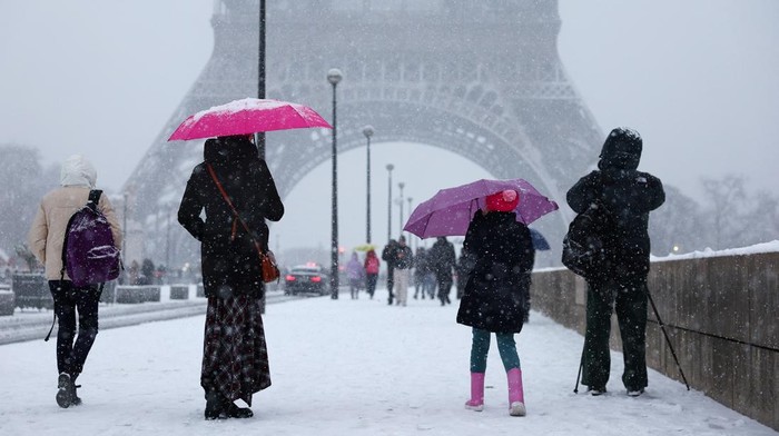 People walk under umbrellas in the snow near the Eiffel Tower in Paris, as winter weather with snow and cold temperatures hits a large part of the country, France, January 5, 2026. REUTERS/Abdul Saboor
