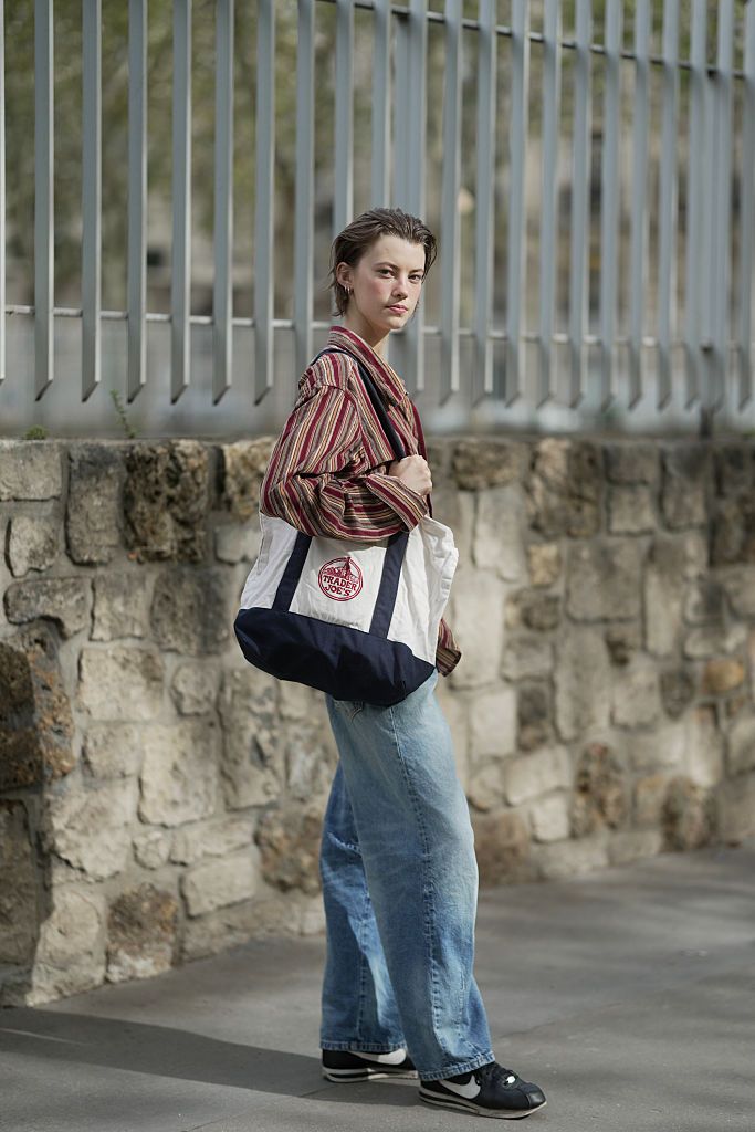 PARIS, FRANCE - OCTOBER 02: Dana Smith is seen wearing short, slicked-back hair, gold hoop earrings, a relaxed-fit multicolored vertical striped shirt, wide-leg light blue jeans, Nike black sneakers, and carrying a Trader Joe's tote bag outside Rabanne during the Womenswear Spring Summer 2026 as part of Paris Fashion Week on October 02, 2025 in Paris, France. (Photo by 305pics/Getty Images)