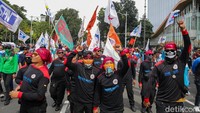 Para buruh mengibarkan bendera serikat, membawa poster, serta membentangkan spanduk berisi tuntutan kenaikan upah.
