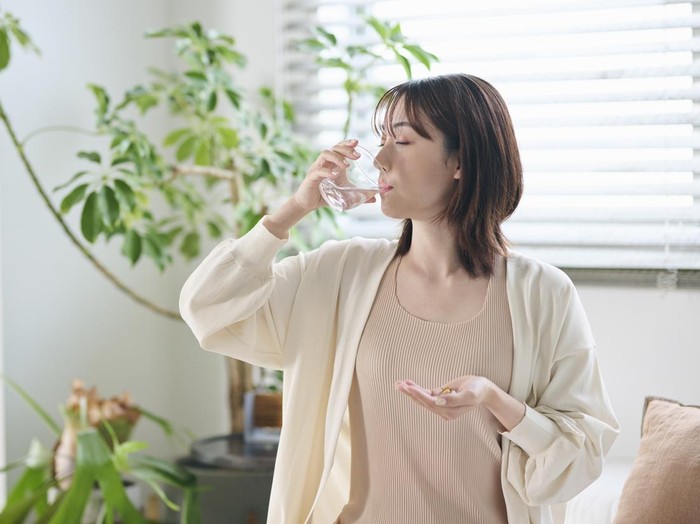 A 20-something woman taking a supplement in bed