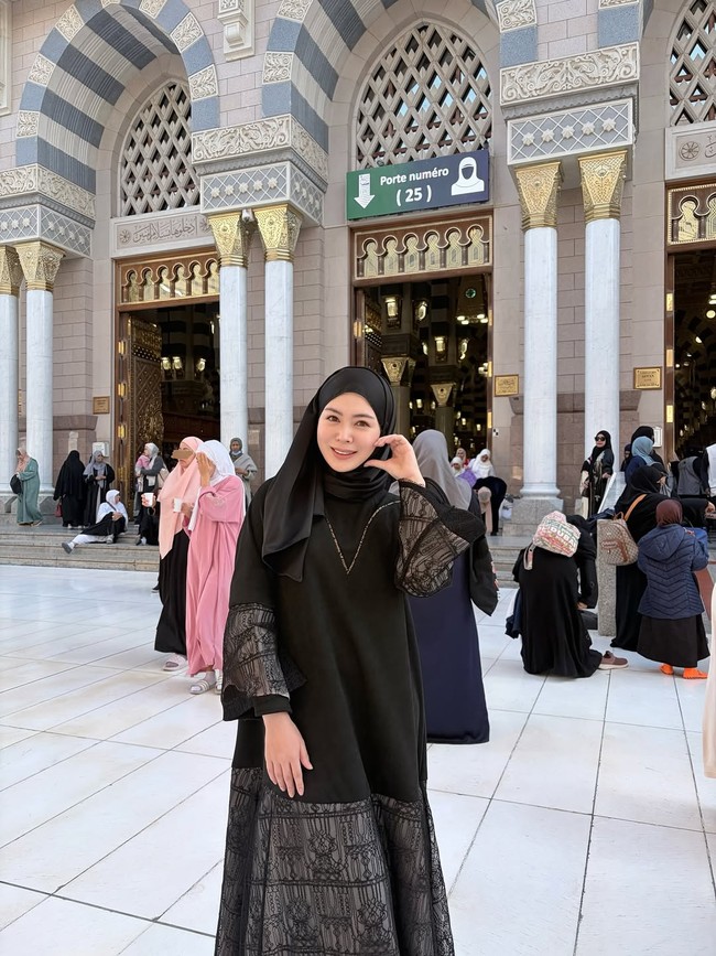 Berpose di depan pintu gerbang masjid Nabawi, Ayana menggunakan hijab pashmina hitam yang disampirkan salah satu sisinya ke bahu. Perpaduan antara hijab gelap dan gamis senada dengan detail renda di bagian bawah membuat penampilannya terlihat sopan dan simpel. Foto: Dok. Instagram @xolovelyayana.