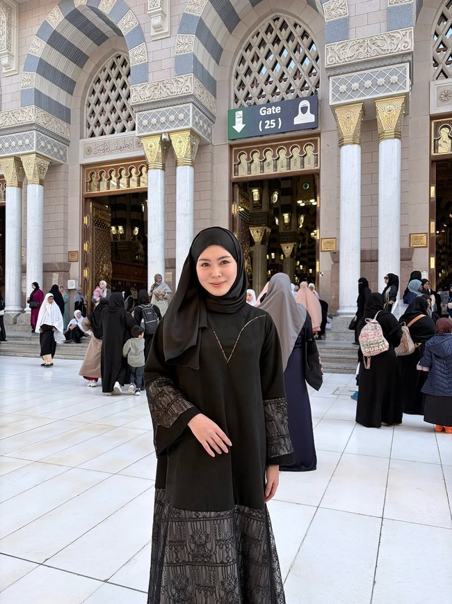 Wanita asal Korea Selatan ini mengenakan hijab pashmina hitam yang dililit rapi, dipadukan dengan gamis hitam berhias aksen renda transparan pada bagian lengan. Penampilannya terlihat elegan saat berpose di koridor masjid. Foto: Dok. Instagram @xolovelyayana.