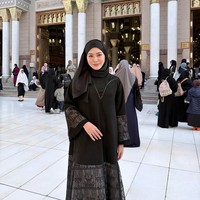 Wanita asal Korea Selatan ini mengenakan hijab pashmina hitam yang dililit rapi, dipadukan dengan gamis hitam berhias aksen renda transparan pada bagian lengan. Penampilannya terlihat elegan saat berpose di koridor masjid. Foto: Dok. Instagram @xolovelyayana.