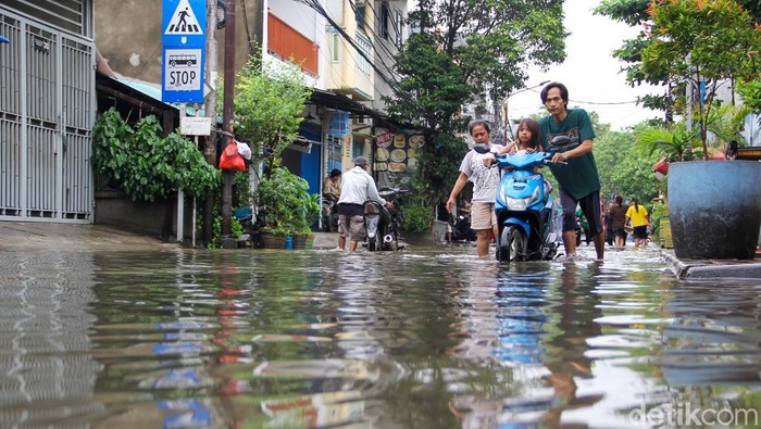 Pengendara motor mendorong kendaraannya saat melintasi genangan banjir di Jl Pademangan VI, Pademangan Timur, Jakarta Utara, Senin (12/1/2026).