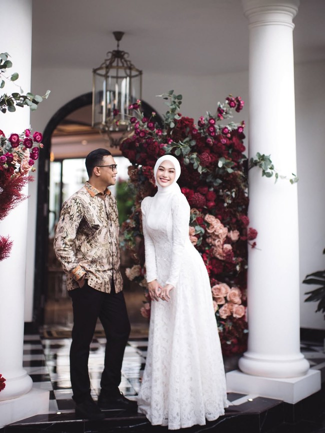 Wanita kelahiran 18 Juni 1993 ini memilih dekorasi floral yang mewah. Suasana lamaran semakin elegan dengan latar belakang kain merah marun yang dramatis serta hiasan bunga mawar merah dan peach yang tersusun cantik di antara pilar putih klasik oleh @memulaicerita.  Foto: Dok. Instagram @indahnadapuspita.