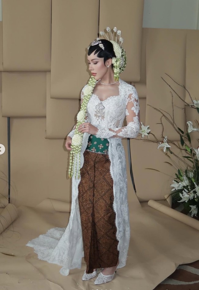 Patricia mengenakan kebaya rancangan desainer Didiet Maulana. Kebaya putih berbahan lace transparan itu dipercantik dengan detail bordir halus. Potongannya fitted mengikuti siluet tubuh, dilengkapi ekor kebaya panjang yang memberi kesan sakral dan mewah khas akad nikah adat Jawa. Foto: Instagram/@rhay_david
