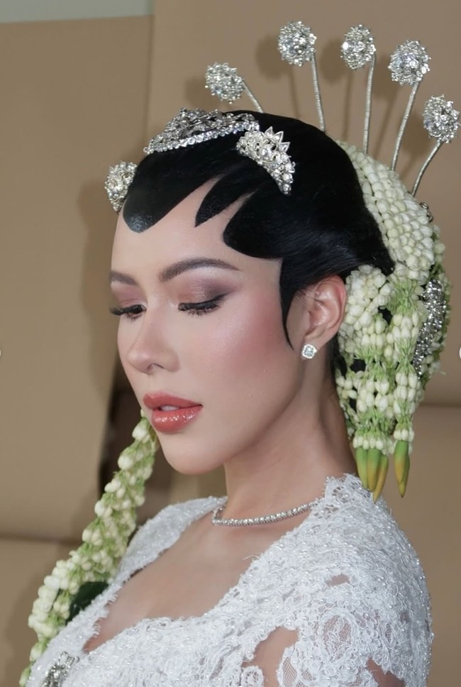 Makeup Patricia tampil flawless dengan complexion halus, blush pink lembut, dan contour tipis yang mempertegas struktur wajah. Riasan mata dibuat soft dengan bulu mata lentik, sementara bibir glossy bernuansa peach-rose memberi kesan segar, feminin, dan menenangkan. Foto: Instagram/@rhay_david