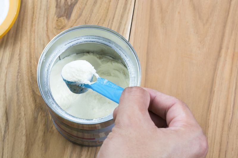 susu formula Powder milk and blue spoon on light background close-up