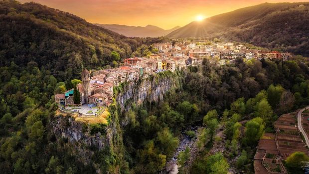 Pemandangan udara desa abad pertengahan Castellfollit de la Roca di tepi tebing saat matahari terbenam di La Garrotxa, Girona, Catalonia, Spanyol.