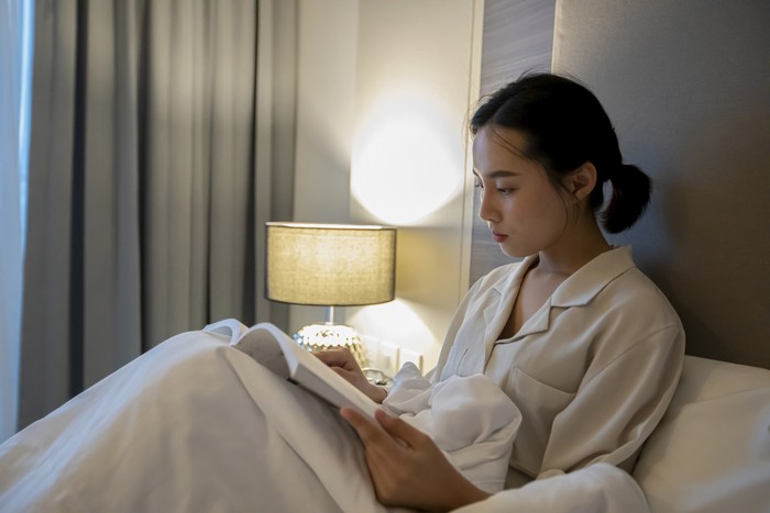 Asian women reading a book and smiling and happy Relaxing in the bedroom at home, she drinking coffee