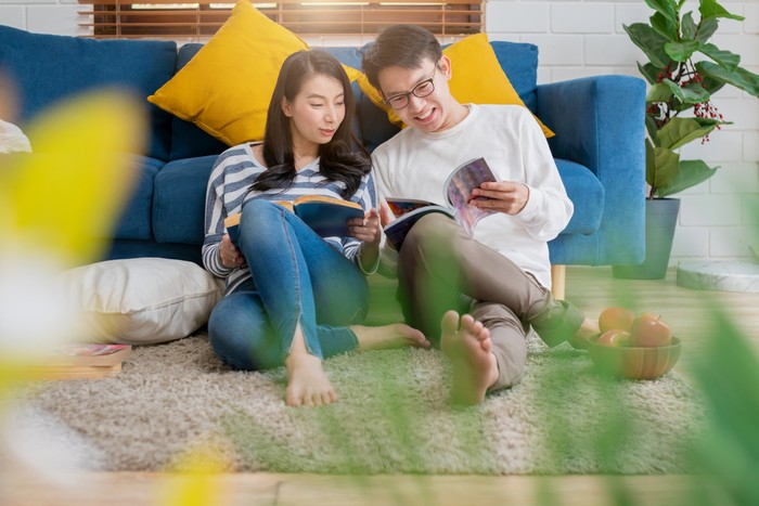 sweet lovey asian family couple sit talk good conversation and read book together next to sofa in living room house background