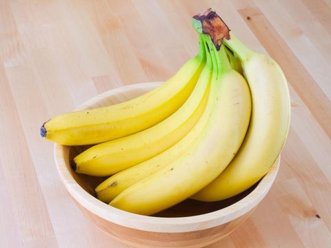 Ilustrasi pisang Bunch of bananas in a wooden bowl on a table.
