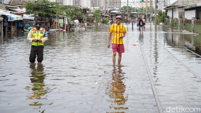 Warga melintas di atas rel kereta api yang terendam banjir di kawasan Kampung Bandan, Jakarta, Minggu (18/1/2026).