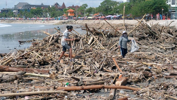 Seorang warga berdiri di atas tumpukan sampah kiriman di Pantai Kuta, Badung, Bali, Senin (19/1/2026). Objek wisata yang menjadi ikon pariwisata Bali tersebut dipenuhi sampah kayu dan bambu yang berserakan di pesisir pantai sejak Minggu (18/1) akibat terbawa ombak dampak cuaca ekstrem. ANTARA FOTO/Nyoman Hendra Wibowo/tom.