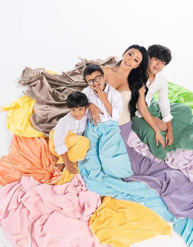 Pada look pertama, konsep yang diusung terlihat playful dan modern dengan sentuhan artistik. Asri Welas dan ketiga putranya tampil berbalut kain berwarna hijau, kuning, ungu, dan biru yang memberi kesan ceria. Foto: Instagram/@riomotret