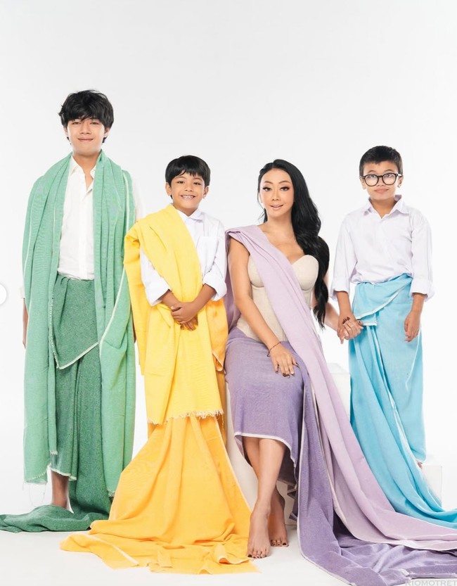 Asri tampil anggun dalam balutan dress nude berpotongan simpel, dipadukan dengan kain ungu lembut yang disampirkan di bahu dan menjuntai hingga lantai. Siluet busananya memberi kesan feminin dan elegan, namun tetap modern. Foto: Instagram/@riomotret