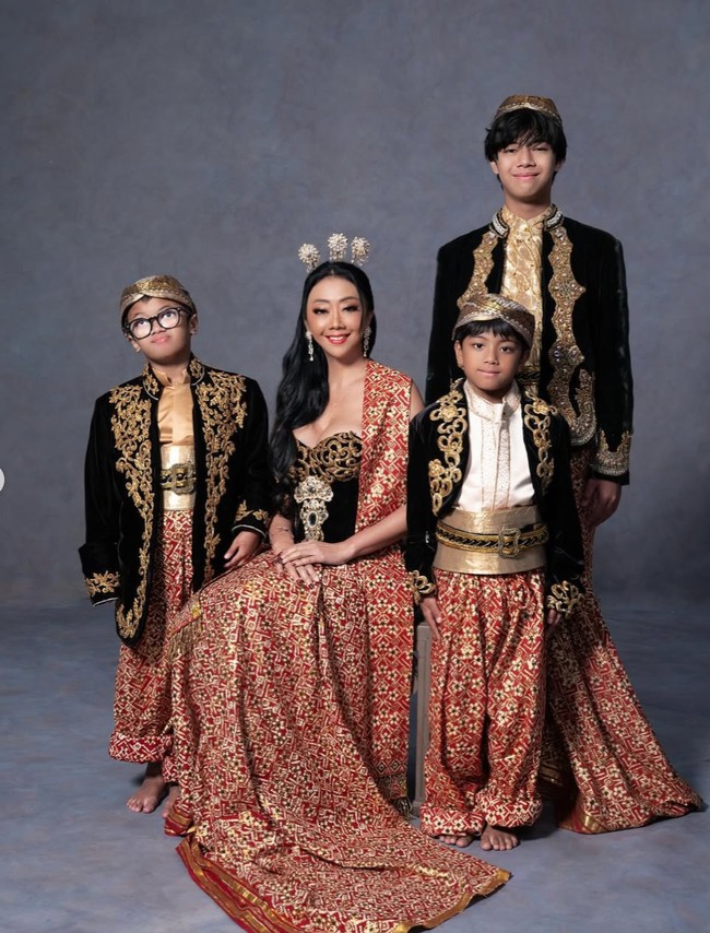 Busana yang dikenakan Asri di kedua look tersebut tampak memiliki potongan dada cukup rendah, memberikan kesan seksi dalam keseluruhan tampilan. Sementara ketiga putranya tampil serasi dalam setelan adat berupa atasan hitam berbordir emas, kain songket merah, serta ikat pinggang emas. Foto: Instagram/@riomotret