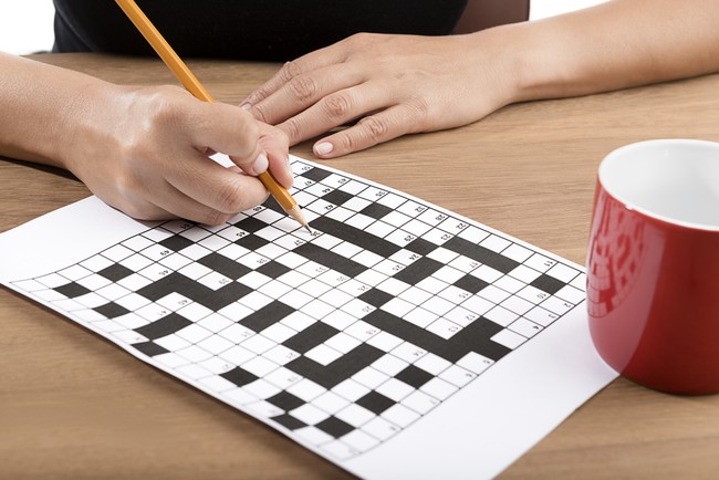 Adult woman solving crossword puzzle with yellow pencil.