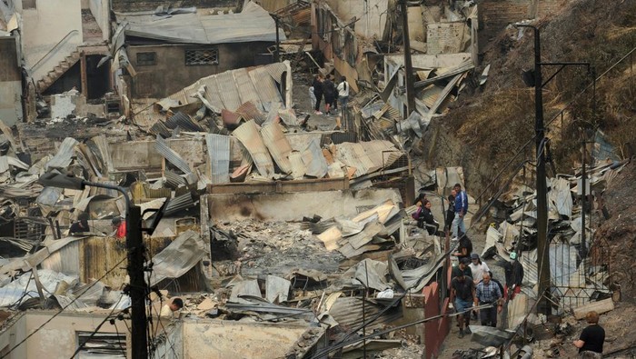 Residents walk among the remains of burnt houses after a wildfire destroyed hundreds of properties, killed several people and forced mass evacuations, while authorities continue battling nearly two dozen blazes intensified by extreme heat and high winds, in Lirquen, Chile, January 19, 2026. REUTERS/Jose Luis Saavedra     TPX IMAGES OF THE DAY
