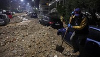 Seorang warga membersihkan puing-puing di samping sebuah mobil di kawasan Glyfada, pinggiran Athena, Yunani, Rabu (21/01/2026). REUTERS/Louisa Gouliamaki  