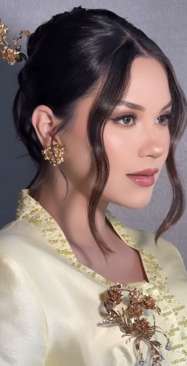 Rambut Alyssa ditata dalam sanggul rapi bergaya modern dengan belahan tengah. Dua helaian rambut yang dibiarkan menjuntai di sisi wajah memberi sentuhan soft dan romantis, memperhalus garis wajahnya. Foto: Instagram/@alyssadaguise/@bennusorumba