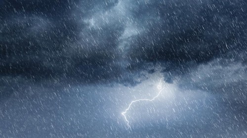 This intense weather scene captures the raw power of nature with storm clouds billowing across an overcast sky, heavy rainfall, and flashes of lightning illuminating the dark atmosphere. The dramatic, moody sky and cascading raindrops evoke a sense of powerful energy and impending force, perfect for visualizing extreme weather conditions. The composition showcases a blend of ominous clouds and heavy rain, ideal for projects focusing on nature, meteorology, or environmental themes.