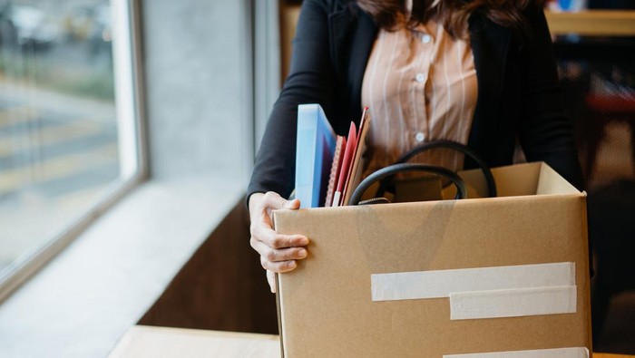 Asian woman holding cardboard box containing personal belongings after being fired by employer