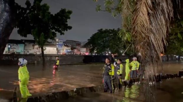 Personel Ditlantas Polda Metro Jaya melakukan pengaturan lalu lintas di jalan yang terendam banjir, Kamis (22/1/2026) malam.