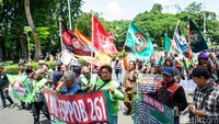 Spanduk bertuliskan tuntutan realisasi Perpres Ojol dibentangkan oleh massa aksi di pagar pembatas yang dipasang aparat kepolisian.