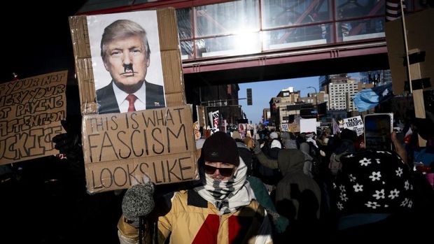 Aksi protes meluas setelah penembakan fatal oleh agen ICE yang menewaskan seorang pria di Minneapolis, AS A person holds a This Is What Fascism Looks Like sign featuring a photo of Donald Trump with a Hitler-style mustache as people march during the