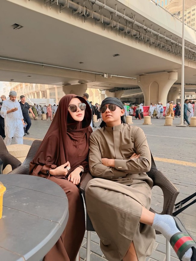 Saat bersantai bersama suami di sela-sela ibadah di Tanag Suci, ia memilih hijab model bergo berwarna cokelat tua yang senada dengan gamisnya. Tampilan earth tone ini dipermanis dengan penggunaan kacamata hitam, memberikan kesan modern namun tetap syari. Foto: Dok. Instagram @bellabonita_r.a.