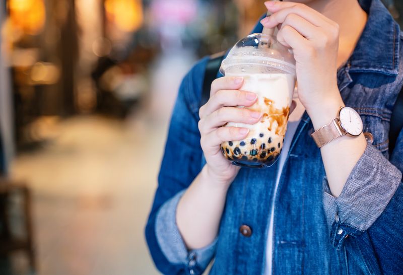 Ilustrasi minum boba Young girl in denim jacket is drinking brown sugar flavored tapioca pearl bubble milk tea with glass straw in night market of Taiwan, close up, bokeh