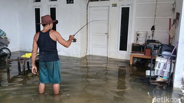 Di tengah banjir, Kastiman memancing ikan pada sebuah teras rumah warga, Rabu (28/1/2026) siang.
