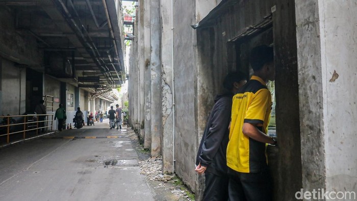 Dua pekerja membeli makanan dan minuman melalui lubang kecil di tembok pembatas kawasan permukiman dan pusat perbelanjaan di Kemang, Jakarta, Selasa (31/1/2026).