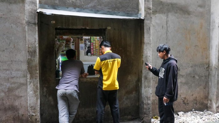 Dua pekerja membeli makanan dan minuman melalui lubang kecil di tembok pembatas kawasan permukiman dan pusat perbelanjaan di Kemang, Jakarta, Selasa (31/1/2026).