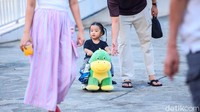 Seorang anak didampingi orang tuanya menikmati waktu santai berkeliling taman. Lapangan Banteng kerap dimanfaatkan keluarga untuk berjalan santai tanpa agenda khusus, cukup menikmati suasana hijau di pusat kota.