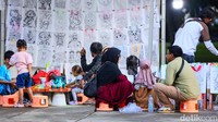 Anak-anak melakukan kegiatan menggambar di area taman, sementara orang tua menunggu di sekitar lokasi. Banyak pengunjung datang tanpa rencana khusus, menjadikan taman ini tempat ideal untuk bersantai di akhir pekan.