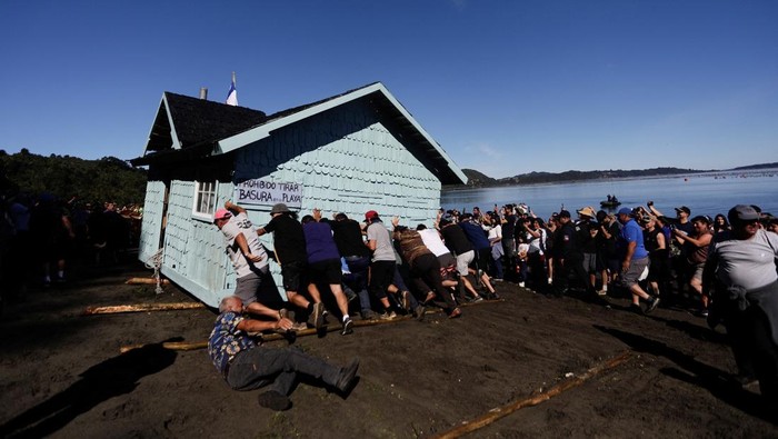 Locals and tourists pull a house which was previously floated with air buoys and brought through the water fastened to a boat during a communal practice on Chile's Chiloe archipelago, called Minga, where neighbors collaboratively move a wooden house to a new location, at Lemuy island, Chile, January 31, 2026. REUTERS/Amilix Fornerod     TPX IMAGES OF THE DAY