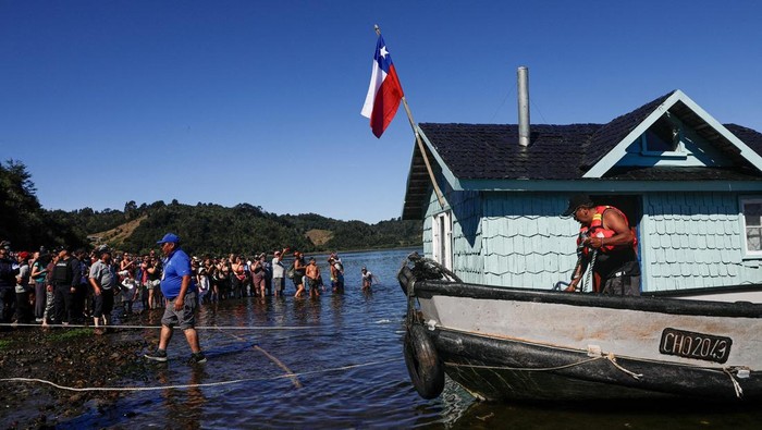 Locals and tourists pull a house which was previously floated with air buoys and brought through the water fastened to a boat during a communal practice on Chile's Chiloe archipelago, called Minga, where neighbors collaboratively move a wooden house to a new location, at Lemuy island, Chile, January 31, 2026. REUTERS/Amilix Fornerod     TPX IMAGES OF THE DAY
