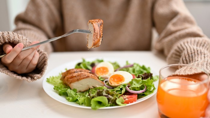 Cropped image, Diet woman eating a fresh healthy salad with grilled chicken breast or chicken fillet and orange juice at the dining table.