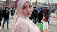 Finazia jalan-jalan ke Universal Studios Jepang. Ia memakai kardigan pink dengan hijab berwarna senada, serta memakai bando berkarakter, juga sambil dua tangannya memegang makanan. (Foto: dok Instagram finazia)