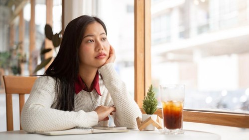 An asian woman is putting her hand under the chin, looking bored or unhappy while waiting for someone at the round marble table. Study or Working in the cafe.