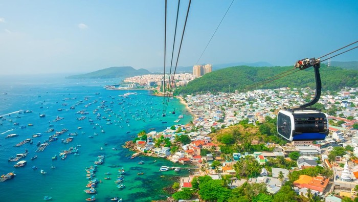 Aerial view of coastal fishermen village with colorful houses, fishing boats, turquoise sea and modern cable car ride on Phu Quoc island, Vietnam. Modern Hon Thom cable car cabin. Tourism infrastructure