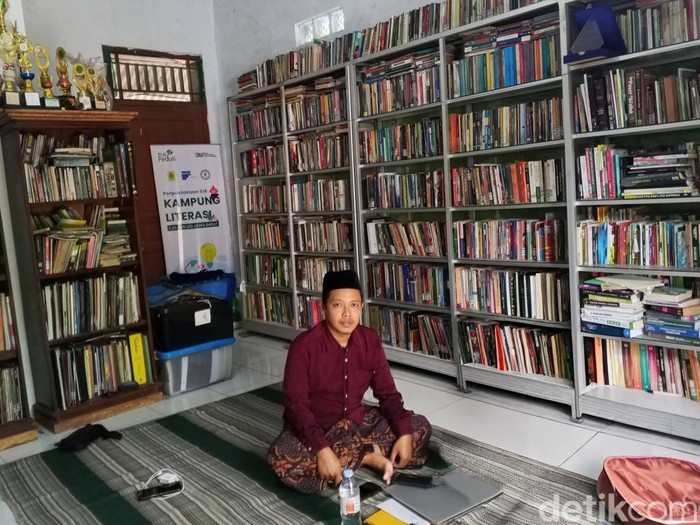 Ahmad Khoeri sedang duduk di depan rak berisi ribuan judul buku, di Perpustakaan S16