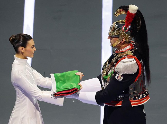 Ceretti menyerahkan bendera Italia kepada penjaga kehormatan Carabinieri, Corazzieri, setelah tampil mengenakan setelan putih, merah, dan hijau yang merepresentasikan warna bendera negaranya. Foto: Getty Images/Elsa